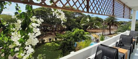 A balcony with a view of a pool and lush greenery, including white flowering plants.