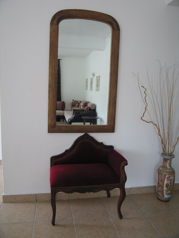 A room with a large mirror, a red velvet bench, and a decorative vase.