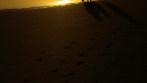 A beach scene with footprints leading towards the ocean, under a sunset sky. - Villa Osumare (Flic-en-Flac)