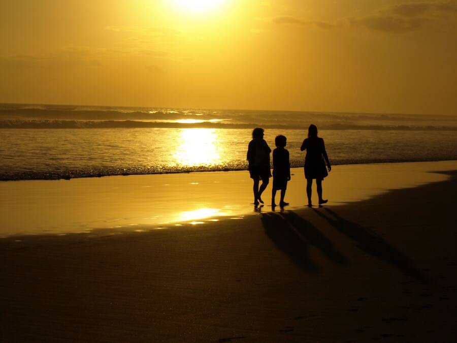 A beach scene with footprints leading towards the ocean, under a sunset sky.