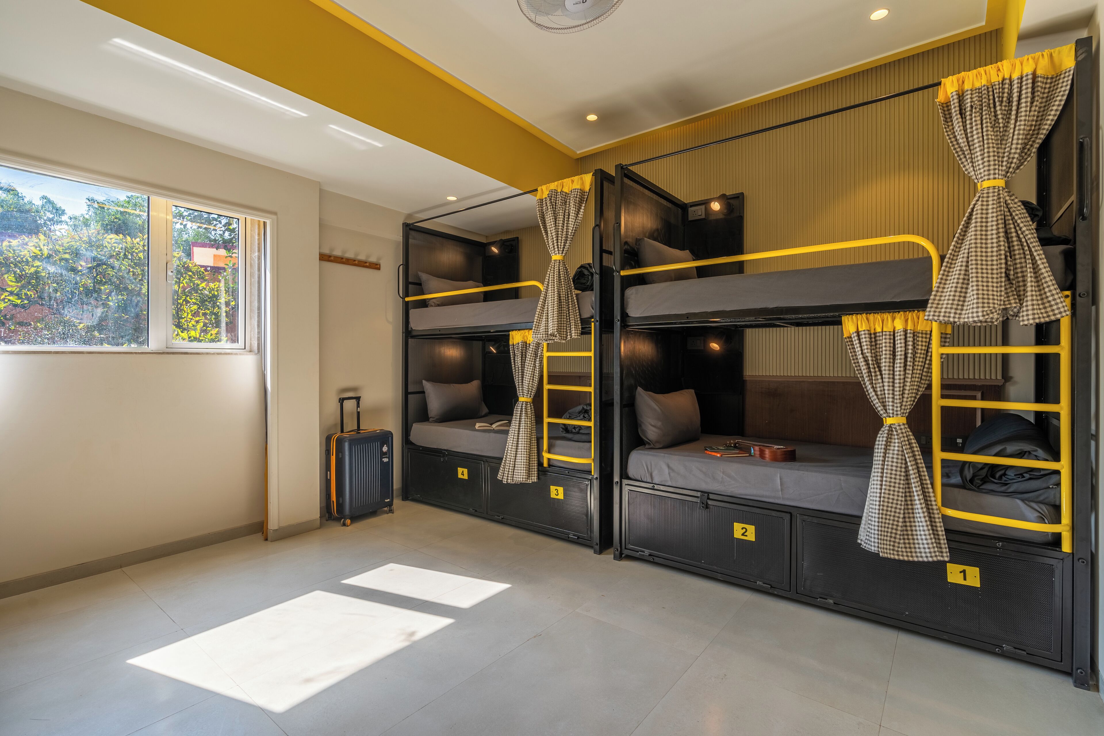 Un dormitorio tipo dormitorio con dos literas, una maleta y una ventana con cortinas.