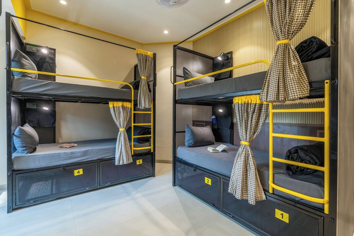 A bunk bed room with yellow railings, checkered curtains, and numbered compartments.