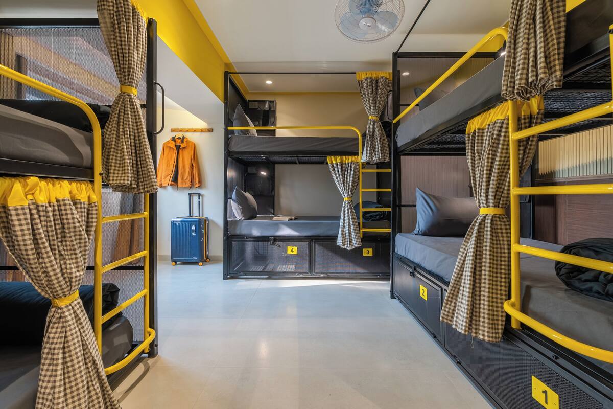 A dormitory room with bunk beds, a desk, a chair, a suitcase, and a fan.