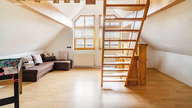 Een slaapkamer met hoge plafonds, bereikbaar via een houten trap, een bank, een tafelvoetbaltafel en dakramen.