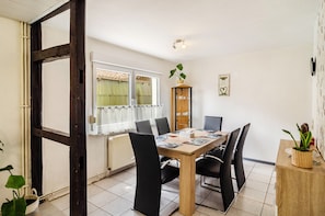 Ein Essbereich mit Holztisch, schwarzen Stühlen, einer Heizung, einem Fenster mit Vorhängen und einem Schrank mit Pflanze.
