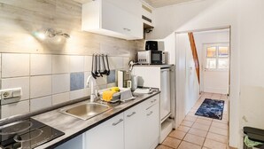 Een keuken met een ingebouwde magnetron, een spoelbak en een fornuis. Er is een raam met gordijnen, een deur die naar een andere kamer leidt, en een betegelde spatwand.