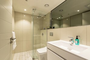 A modern bathroom with a glass shower enclosure, a white sink with a soap dispenser, and a mirror above the sink. - The Docklands Two Bed Superior Apartment (Cape Town)