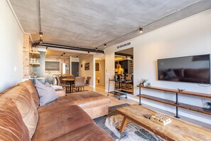 A modern living room with a large sectional sofa, a wooden coffee table, and a flat-screen TV mounted on the wall. - The Docklands Two Bed Superior Apartment (Cape Town)
