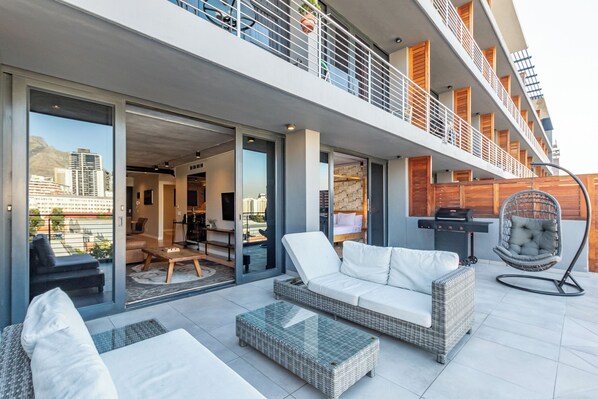 A modern outdoor living area with a sofa, chairs, and a grill. - The Docklands Two Bed Superior Apartment (Cape Town)