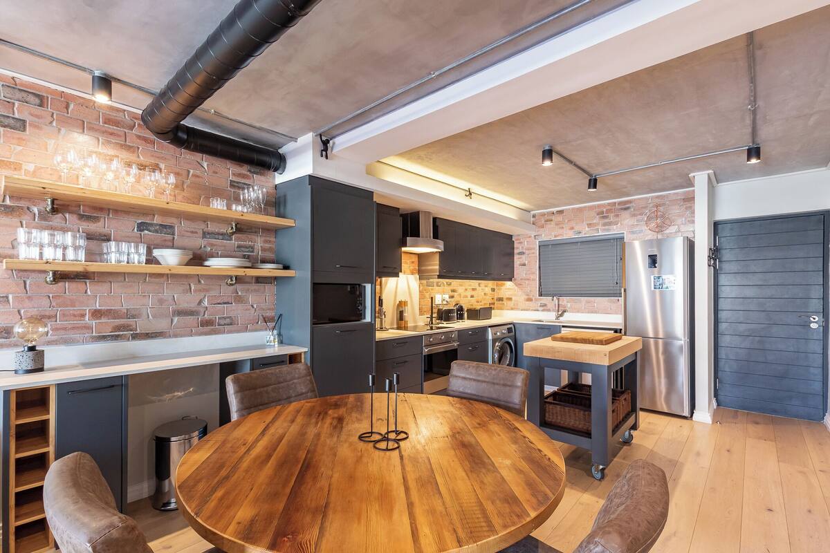 Una cocina moderna con pared de ladrillo, estantes de madera y una mesa redonda de madera.