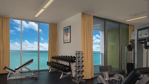 Un gimnasio con vistas al océano, equipo de ejercicios y ventanas amplias.