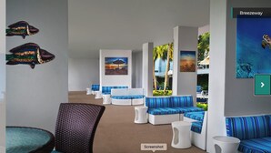 Un área de descanso moderna con asientos a rayas azul y blanco, un ventanal con vista a palmeras y obras de arte en las paredes.