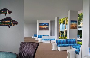 A modern lounge area with striped blue and white seating, a large window with a view of palm trees, and artwork on the walls. - Marriott Crystal Shores 2-bedroom Getaway Marco Island June 27-29 (Marco Island)