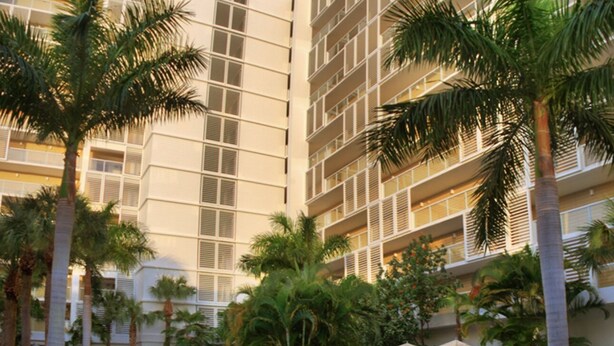 Un hotel de varios pisos con diseño arquitectónico moderno, que cuenta con balcones y palmeras.