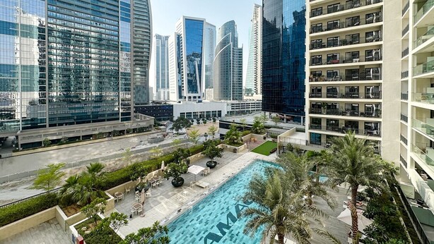 Un hotel moderno in città, con piscina sul tetto, circondato da grattacieli e palme.