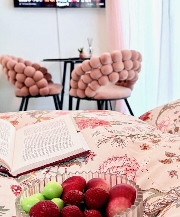 A bed with a floral bedspread, a bowl of fruit, and a book on a bedside table.
