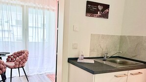 A compact kitchen with a sink, a dining area with a chair, and a view through a door to a balcony. - Charming apartment | balcony, close to the center, self check-in (Augsburg)