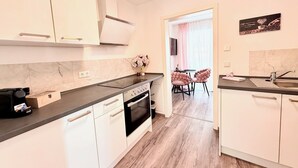 A modern kitchen with white cabinets, a black countertop, and a wooden floor. There is a dining area with pink chairs and a table. - Charming apartment | balcony, close to the center, self check-in (Augsburg)