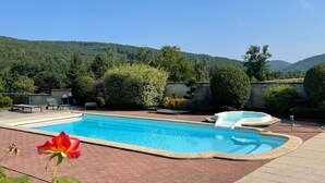 A rectangular swimming pool with a hot tub, surrounded by a brick patio, with a view of a forested hillside. - Aux Fleurs des Champs (Lautenbach)