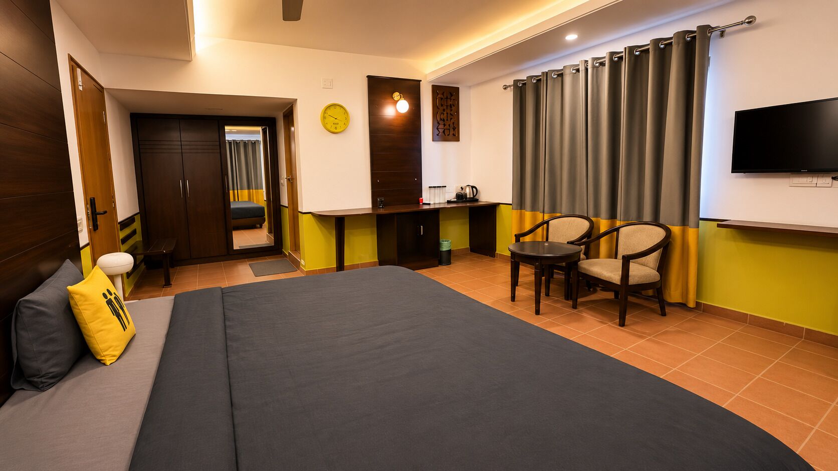 Habitación de hotel con cama, escritorio, silla, televisor y reloj en la pared.