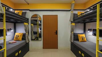 A dormitory room with bunk beds, a wooden door, and a mirror.