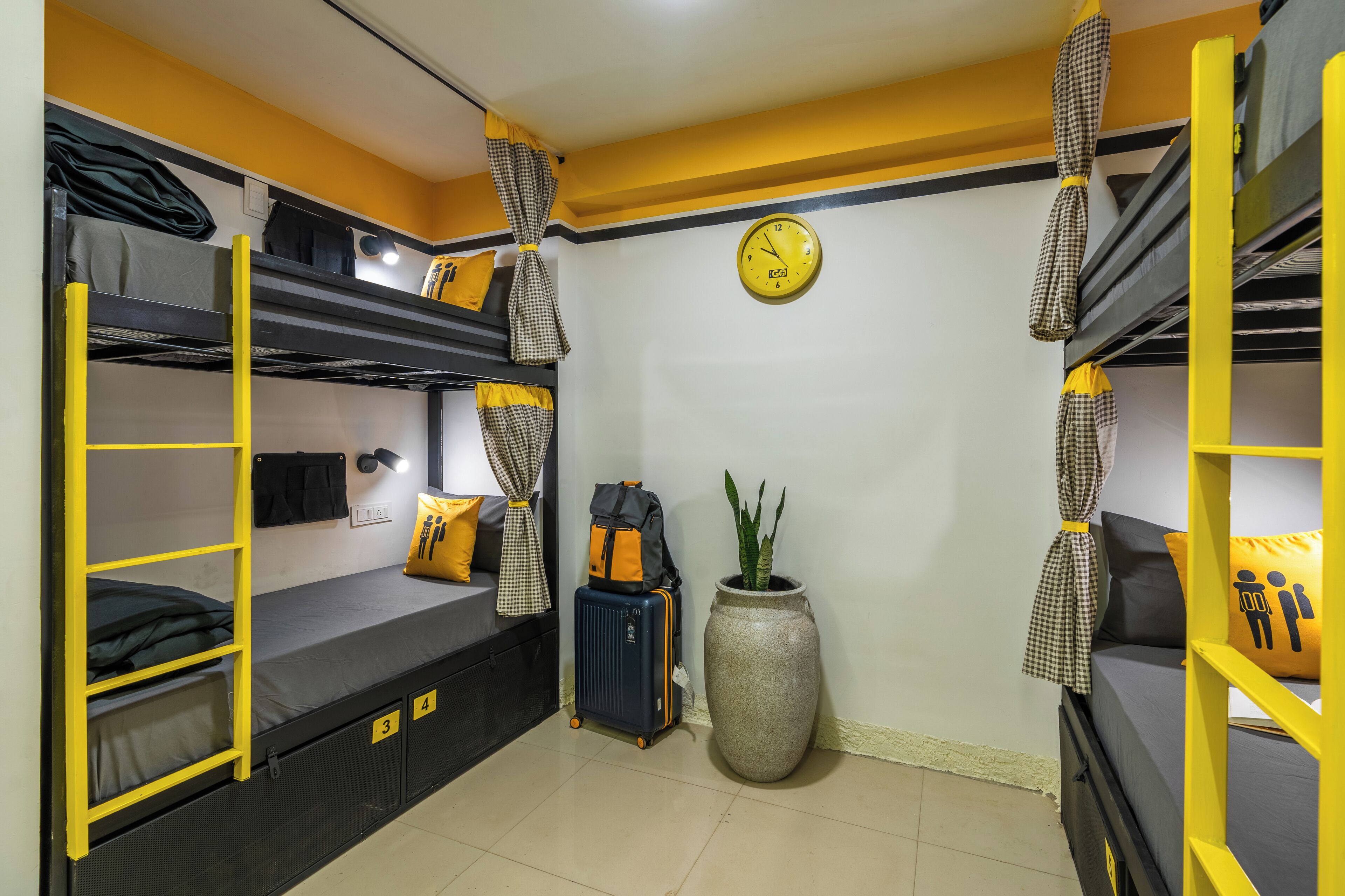 A bunk bed room with a suitcase, a clock, and a potted plant.