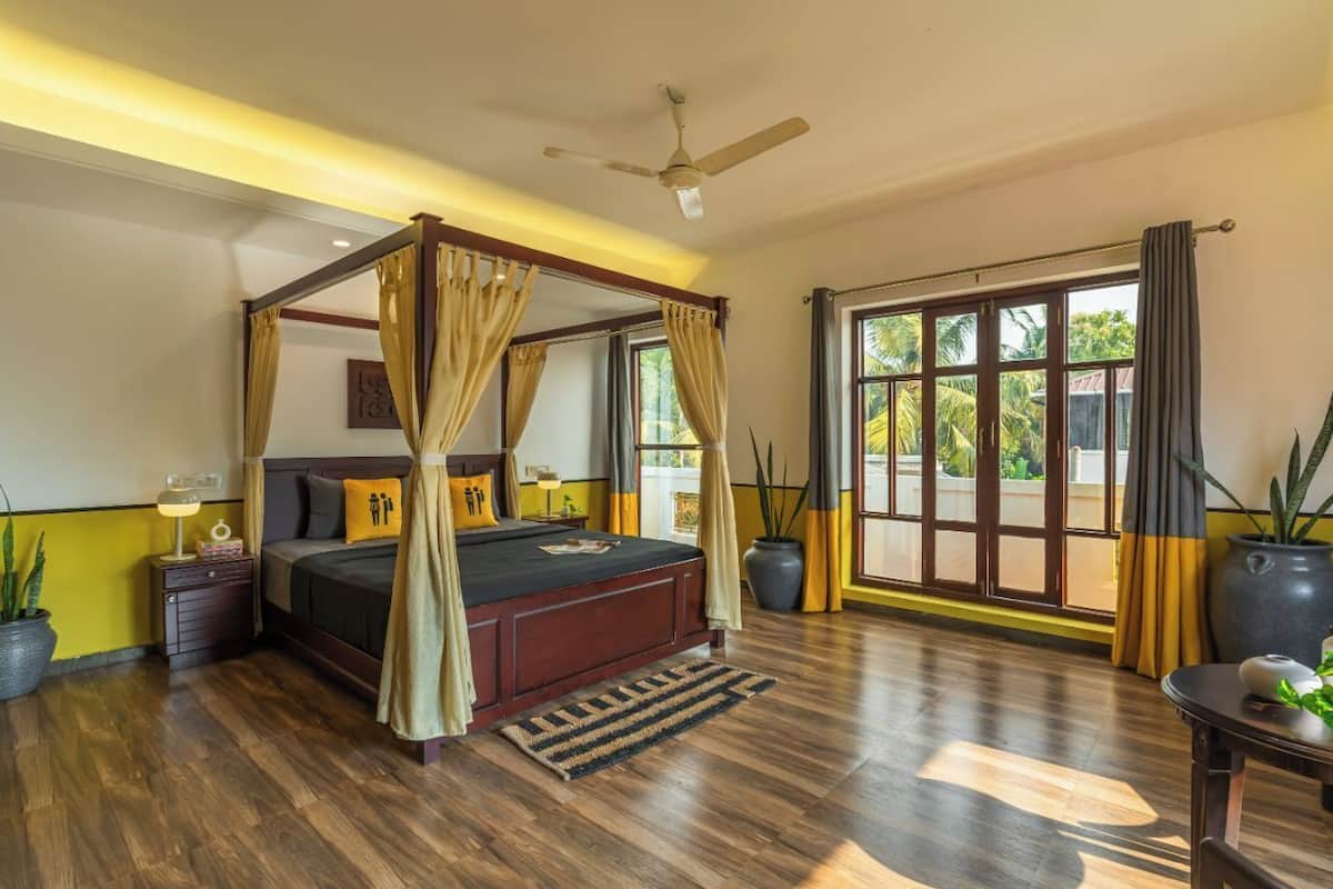 A spacious bedroom with a four-poster bed, a ceiling fan, and large windows with curtains.