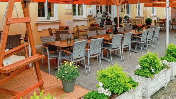 Een terras met tafels en stoelen, een houten ladder en potplanten.