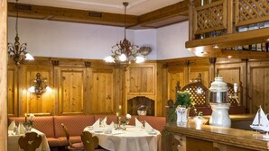 Een traditioneel herberg met houten lambrisering, een centrale eetruimte met ronde tafels en een bar met krukken.