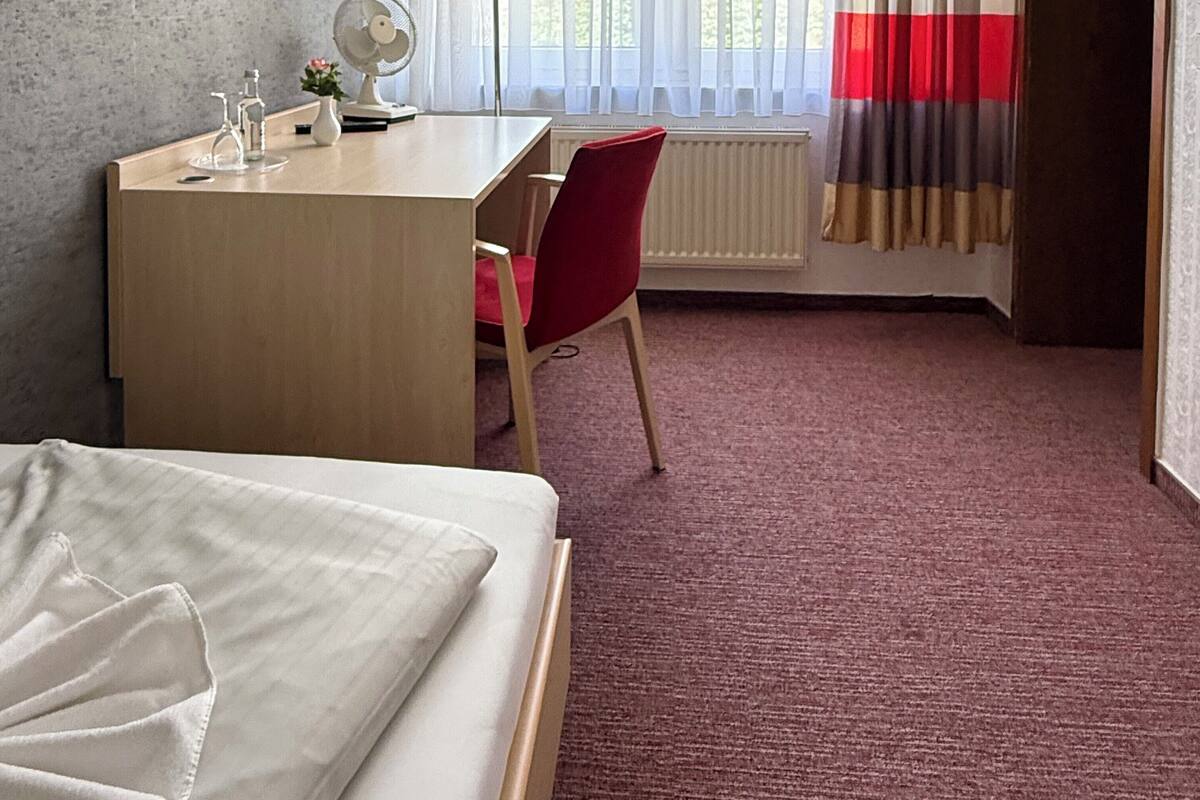Habitación de hotel con cama, escritorio, silla, lámpara y ventana con cortinas.