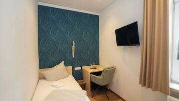 Camera d'albergo con un letto, una scrivania, una sedia, una televisione e una finestra con tende.