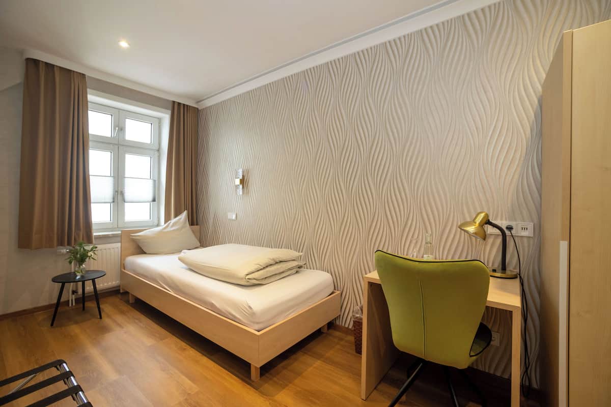 Un dormitorio con cama, un escritorio con silla, una ventana con cortinas y una pared con textura.