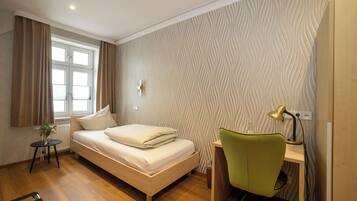 Ein Schlafzimmer mit Bett, Schreibtisch mit Stuhl, Fenster mit Vorhängen und einer strukturierten Wand.