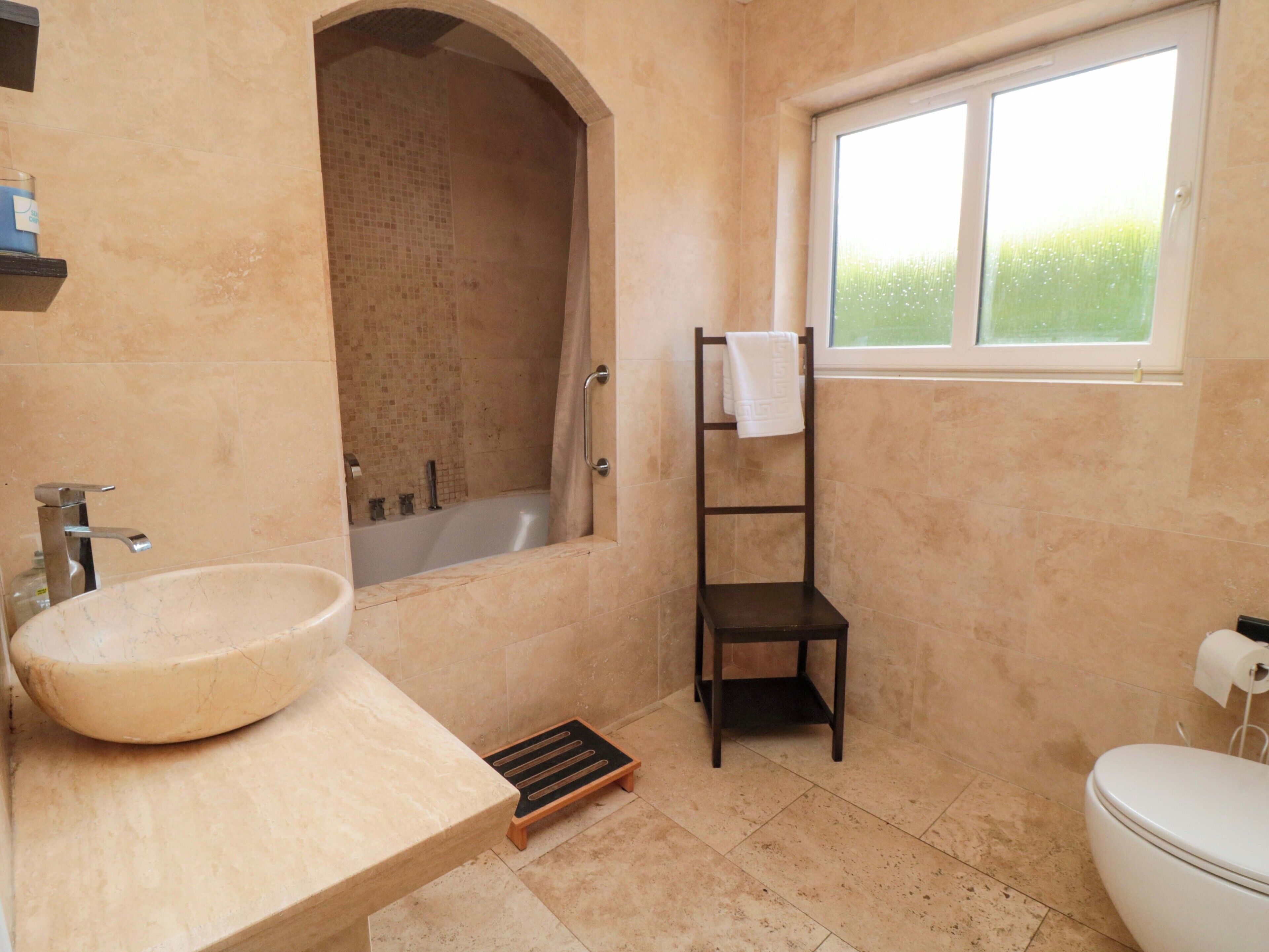 Ein Badezimmer mit einer Badewanne, einem Waschbecken, einem Regal und einem Fenster.