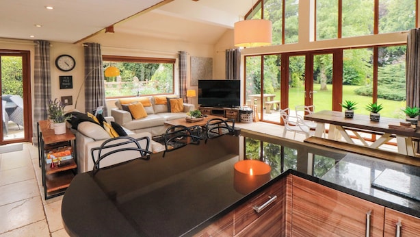 Amplia sala de estar con sofá, mesa de centro y televisor, ventanas grandes que ofrecen vista al jardín.