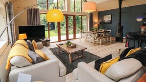 Amplia sala de estar con televisor grande, asientos cómodos, zona de comedor y vistas al exterior.
