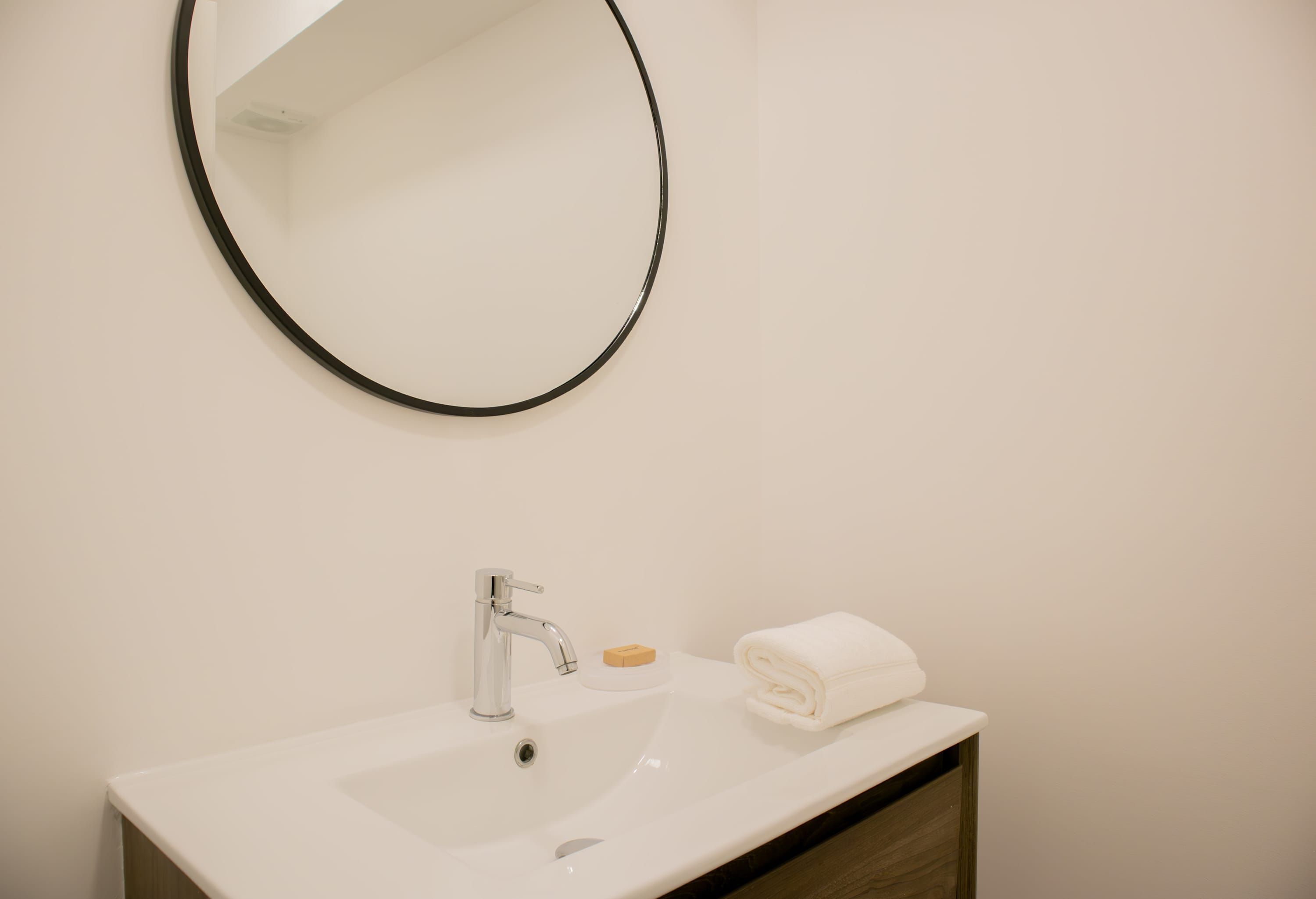 A bathroom with a white sink, a round mirror, a towel, and a soap dish.