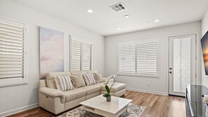 Una sala de estar moderna con un sofá color beige, una mesa de centro blanca y un ventanal con persianas.