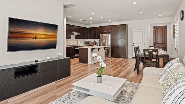 Una sala de estar moderna con un televisor de pantalla plana, una mesa de centro con un florero, un sofá y una zona de comedor con una mesa y sillas.