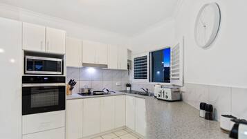 A modern kitchen with white cabinets, a microwave, an oven, a toaster, and a window with blinds.