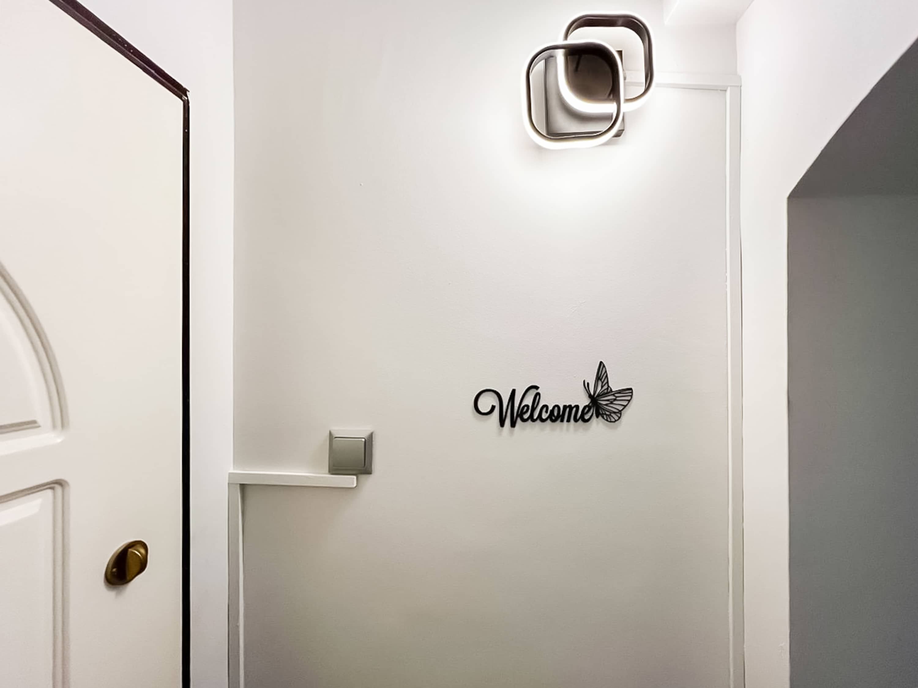 A white door with a brass doorknob, a wall-mounted light fixture, and a 'Welcome' sign with a butterfly decoration.