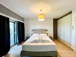 Un dormitorio moderno con una cama grande, una mesita de noche con lámpara, un armario y una ventana con cortinas.