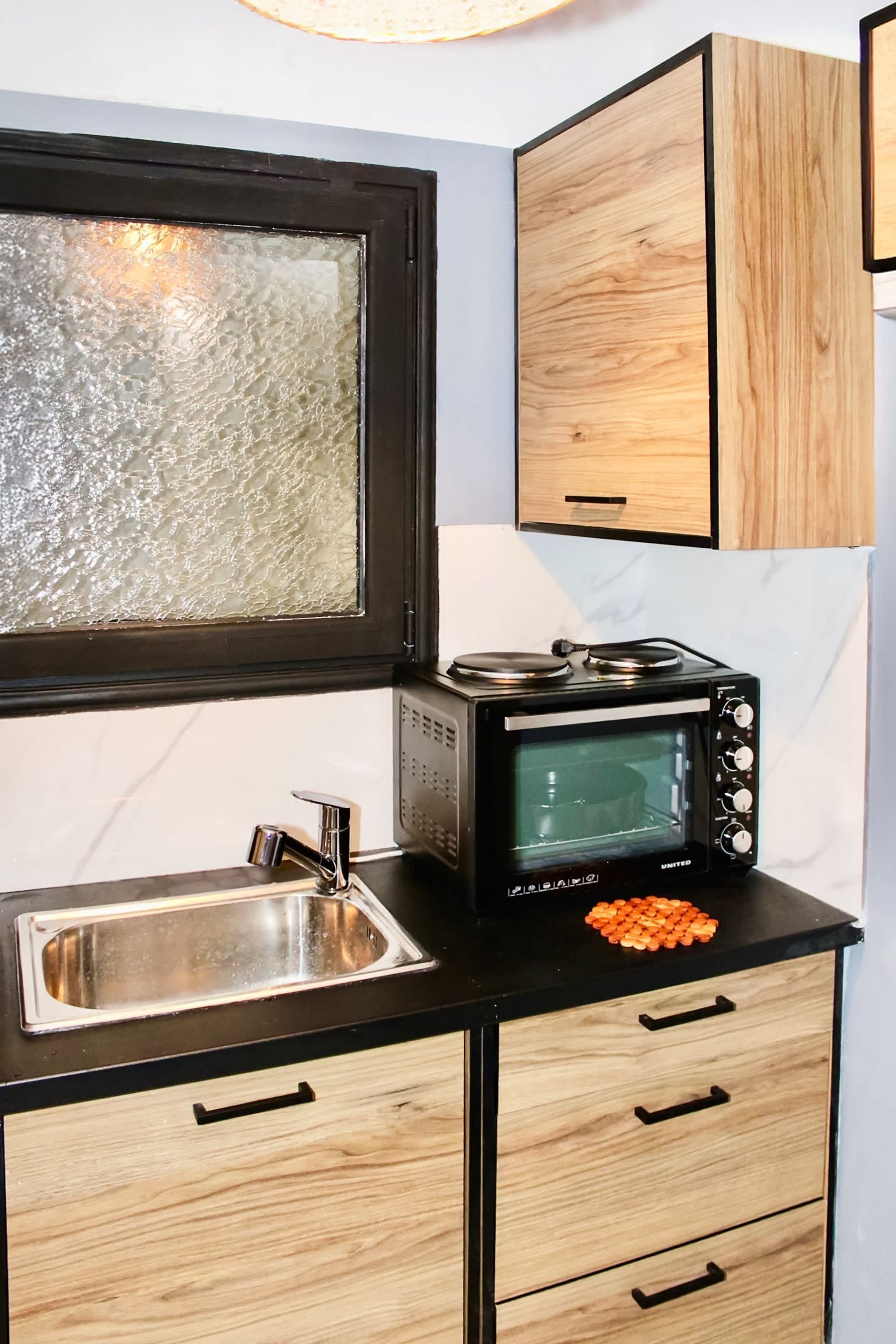 A compact kitchen with a black countertop, a stainless steel sink, a microwave, and wooden cabinets.