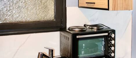 A compact kitchen with a black countertop, a stainless steel sink, a microwave, and wooden cabinets.