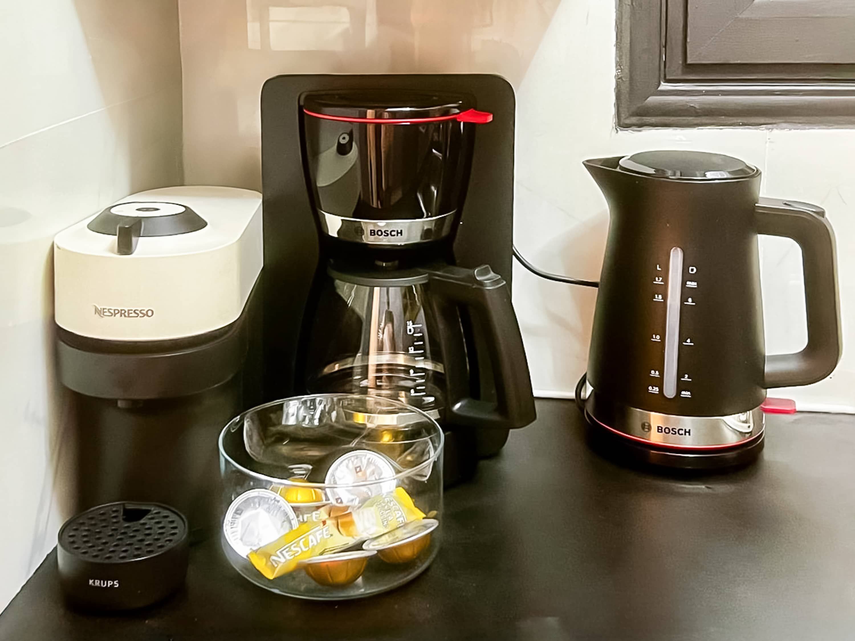Et køkken med kaffemaskine, elkedel, kaffekapselautomat og et glas med kaffekapsler.