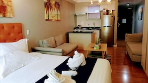A hotel room with a bed, a sofa, a small table with towels, a kitchen area, and a hallway. - Davao Central Suites (Davao)