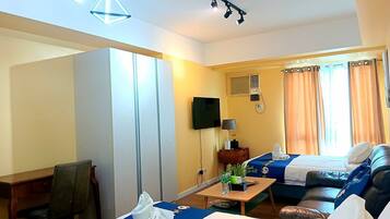 Habitación de hotel con cama, sofá, escritorio, televisor y ventana con cortinas.