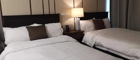Ein Hotelzimmer mit zwei Betten, einem Nachttisch mit Lampe und Blick durch ein Fenster nach draußen.