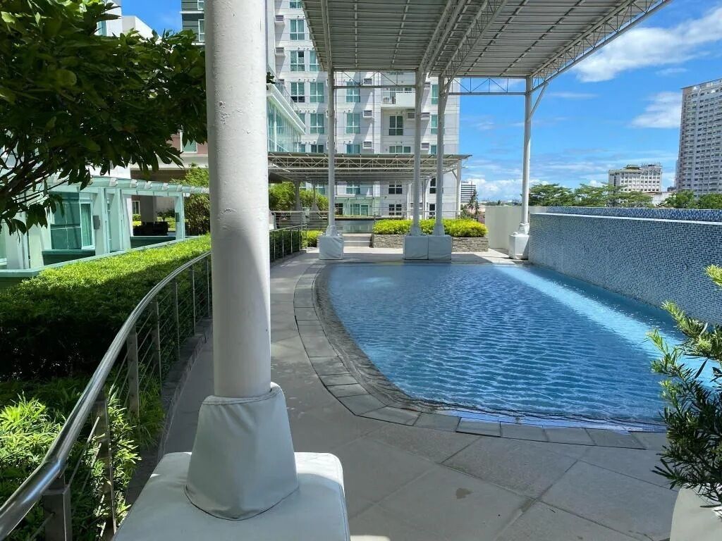 Una piscina en la azotea con barandilla de cristal, rodeada de vegetación y edificios modernos.
