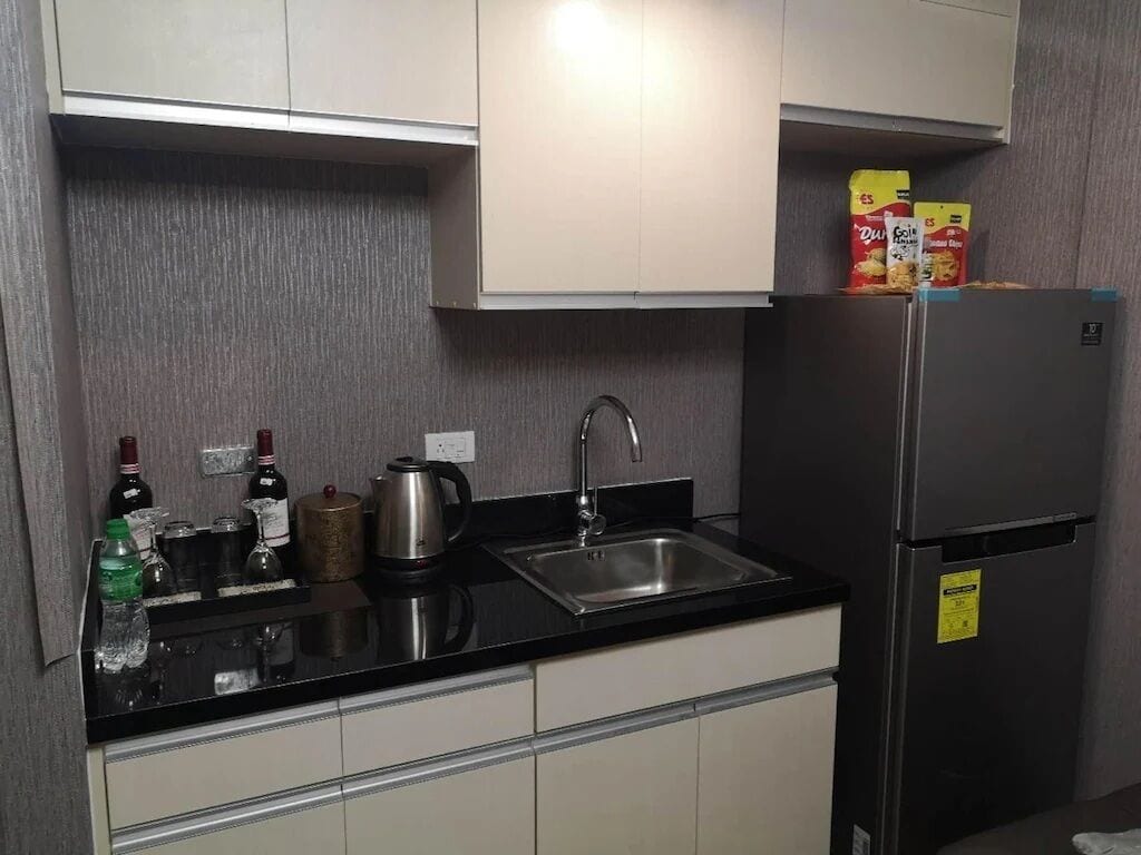 A kitchen with a black countertop, stainless steel sink, and a refrigerator.